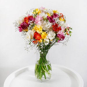Mixed freesia flower bouquet in a clear glass vase, multicolor blooms