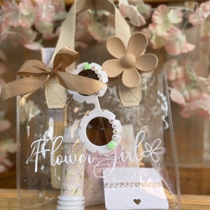Clear flower girl gift bag with white script and flower detail, satin handle, keepsake items