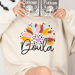 Off-white sweatshirt with colorful floral Doula graphic and 'Doula' text
