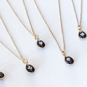 Gold-plated teardrop pendant necklace with tiny pressed flower in dark resin