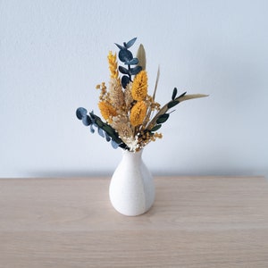 Mini dried floral bouquet in a small white vase with yellow and dark blue stems