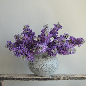 Purple faux lilac branch with clustered blossoms in a gray speckled vase