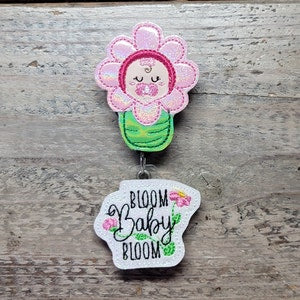 Flower-shaped baby bloom charm with green stem, pink flower, and clip with "Bloom baby" tag