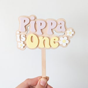 Personalized cake topper on wooden stick, "Pippa is one" with flower accents