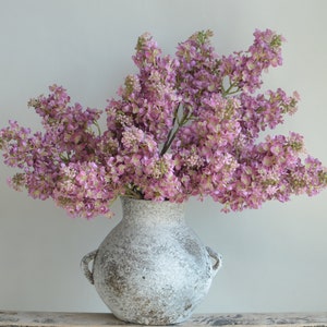 Artificial lilacs branch with mauve pink blossoms in a speckled gray vase