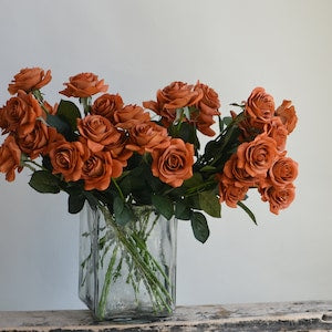 Burnt orange faux rose bouquet with green leaves in clear glass vase