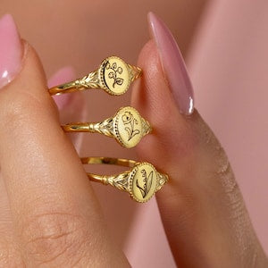 Gold signet ring set with engraved oval birth flower motifs on three fingers