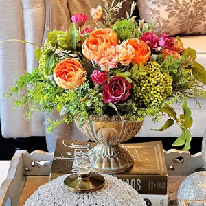 Artificial floral centerpiece in gold metal vase with orange and pink blooms and greenery