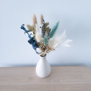 Mini dried floral bouquet in small white vase with blue and white stems