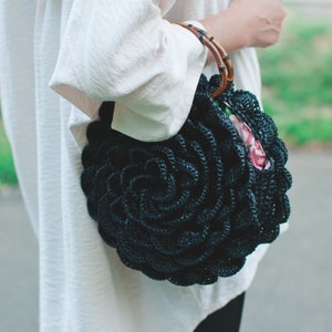 Dark crochet circular bag with layered flower pattern and short top handle