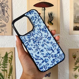 Blue floral patterned phone case with black bumper, held in hand