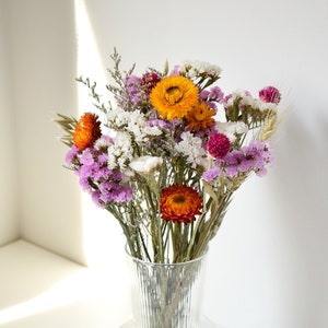 Dried flower bouquet with purple and orange blooms in a clear glass vase