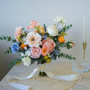 Silk flower bouquet with peach, orange, and blue blooms, greenery, and white ribbon bow