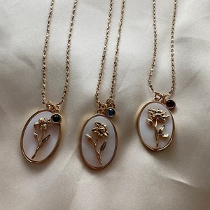 Gold birth flower necklace with three oval pendants, dark stone centers, thin chain