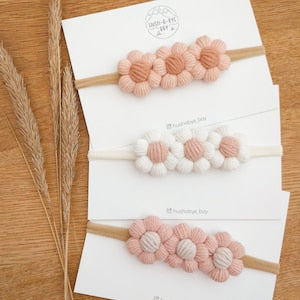 Set of three knitted baby headbands with clustered pink and white flower appliques