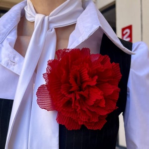 Large red rose brooch pin with ruffled petals on dark fabric