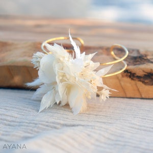Gold-tone bracelet with clustered white dried flowers, adjustable loop closure.