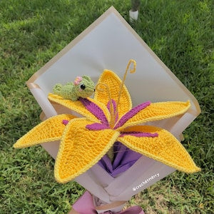Yellow and purple crochet flower decoration with curled petals, on white packaging sheet