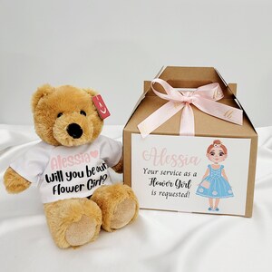 Brown teddy bear wearing a white t-shirt with “Will you be our Flower Girl?” message