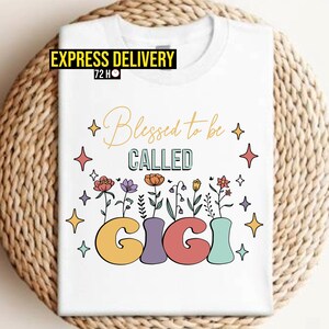 White graphic T-shirt with “Blessed to be called Gigi” text and colorful star floral design