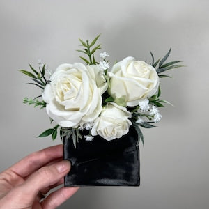 White rose boutonniere in black square pocket with green leaves