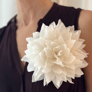 White silk flower brooch with layered petals and center detail, pinned on clothing