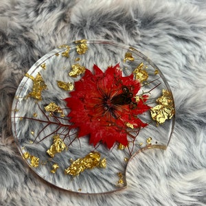 Round glass coaster with red dried flower and gold foil pieces on clear surface