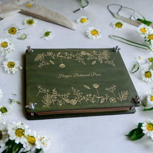 Botanical flower press with dark green cover and gold floral border, hinged metal clamps