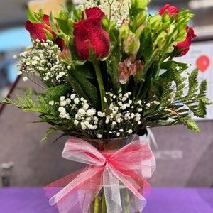 Fresh flower arrangement bouquet with red roses, white baby’s breath, and pink ribbon