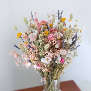 Dried flower bouquet in glass vase with pink, yellow, and lavender blooms and green stems