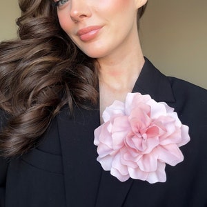 Large pale pink fabric flower brooch on black blazer lapel.