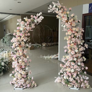 Pale pink flower arch backdrop with dense floral pillar arrangements for outdoor weddings