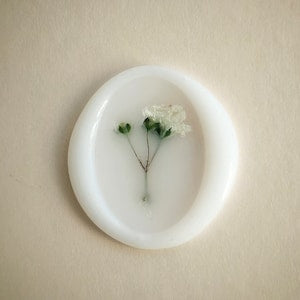 Oval white wax seal sticker with small pressed baby's breath flower