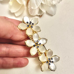 Gold-tone hair clip with three ivory flower petals, blue crystals, and pearl beads