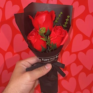 Red rose-shaped soap flower bouquet in black gift wrap with bow and greenery