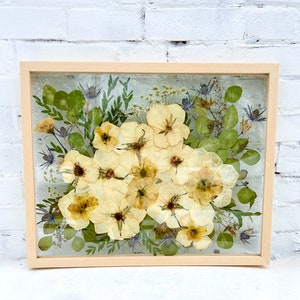Framed preserved bouquet with cream flowers and green leaves in a light wood frame