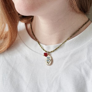 Gold-tone chain necklace with green-blue crystal pendant, bird and mushroom charms