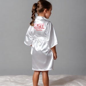 White satin flower girl robe with back lettering and waist tie, knee-length.