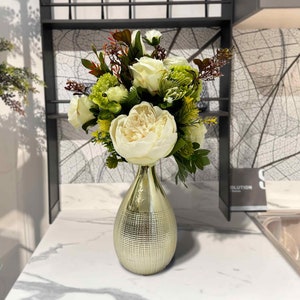 Handmade magnolia flower arrangement with cream blooms and green leaves in gold vase