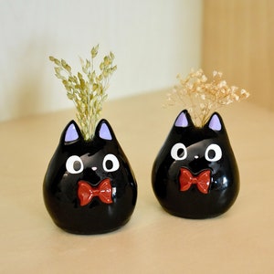 Two small black cat clay figurines with red bow ties and white eyes
