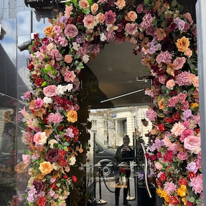 Pink and burgundy flower garland forming a doorway arch with mixed blooms