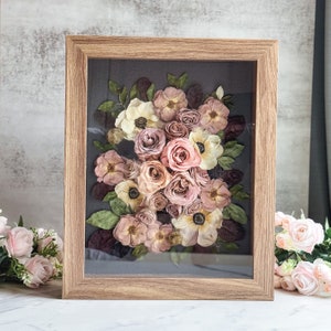 Framed preserved bouquet with pink, cream, and mauve flowers in a light wood frame