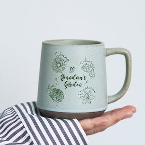 Ceramic coffee mug with garden flower graphic and green printed message, light gray