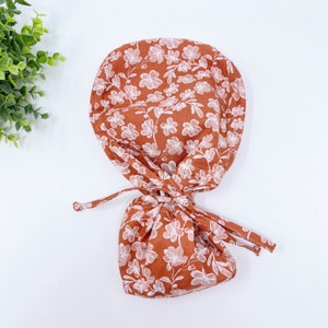 Floral scrub cap with ponytail ties, rust-orange with white flower print