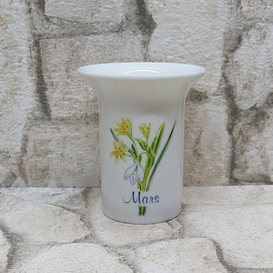White porcelain vase with yellow iris flowers and "Mars" printed near base