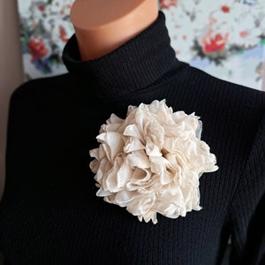 Cream flower brooch pinned to a black sweater collar.