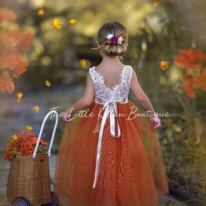 Orange flower girl dress with white lace back yoke and tied ribbon straps, sleeveless