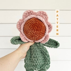 Crochet poppy flower pattern: crocheted flower with pink petals, brown center, green leaves.