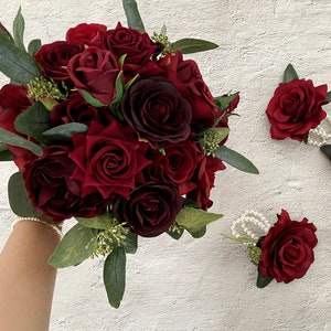 Handheld burgundy rose bouquet with green leaves and small matching rose clusters