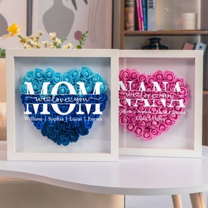 White flower shadow box with two heart-shaped name plaques, blue and pink floral lettering